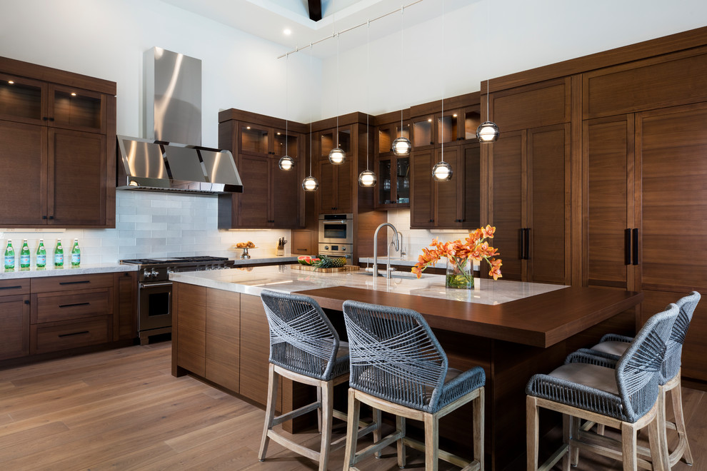 Large world-inspired l-shaped kitchen with engineered stone countertops, integrated appliances, medium hardwood flooring, beige worktops, a submerged sink, shaker cabinets, dark wood cabinets, an island and brown floors.