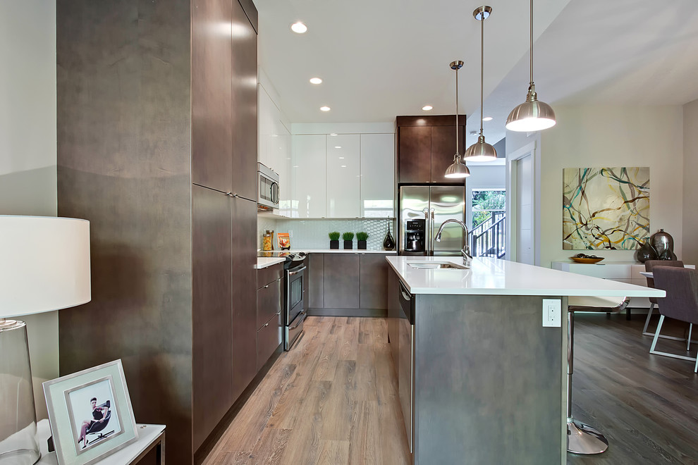Foto på ett mellanstort funkis kök, med en dubbel diskho, släta luckor, grå skåp, bänkskiva i kvarts, vitt stänkskydd, stänkskydd i porslinskakel, rostfria vitvaror, mellanmörkt trägolv och en köksö