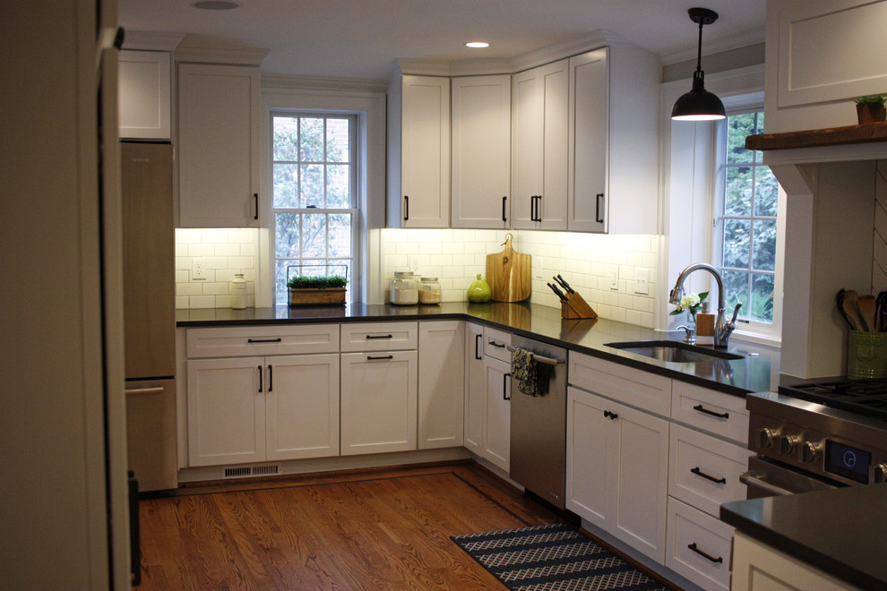 Rural kitchen in Baltimore with white cabinets, metro tiled splashback, stainless steel appliances and brown floors.