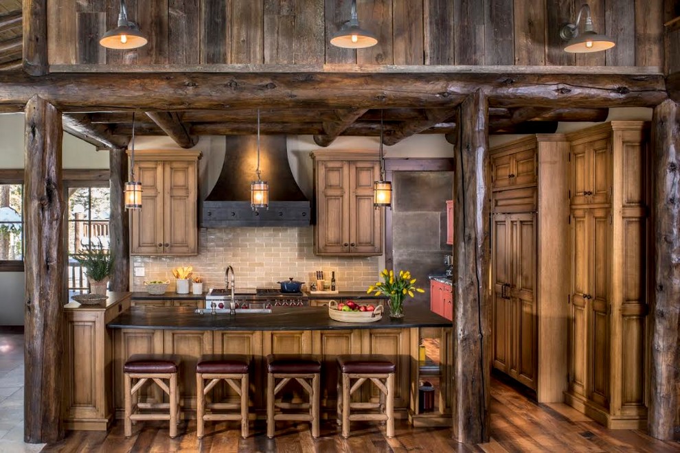 Eat-in kitchen - large rustic l-shaped dark wood floor eat-in kitchen idea in Denver with a farmhouse sink, raised-panel cabinets, medium tone wood cabinets, soapstone countertops, beige backsplash, subway tile backsplash, stainless steel appliances and an island