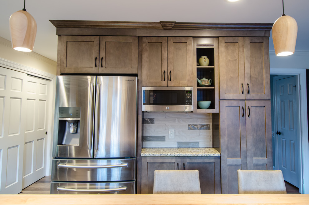 Inspiration for a mid-sized craftsman galley light wood floor open concept kitchen remodel in Raleigh with an undermount sink, recessed-panel cabinets, brown cabinets, granite countertops, beige backsplash, stone slab backsplash, stainless steel appliances and an island