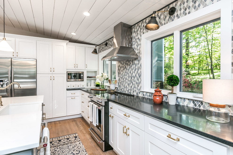 This is an example of a traditional kitchen in Baltimore with a belfast sink, shaker cabinets, grey splashback, stainless steel appliances, light hardwood flooring and an island.
