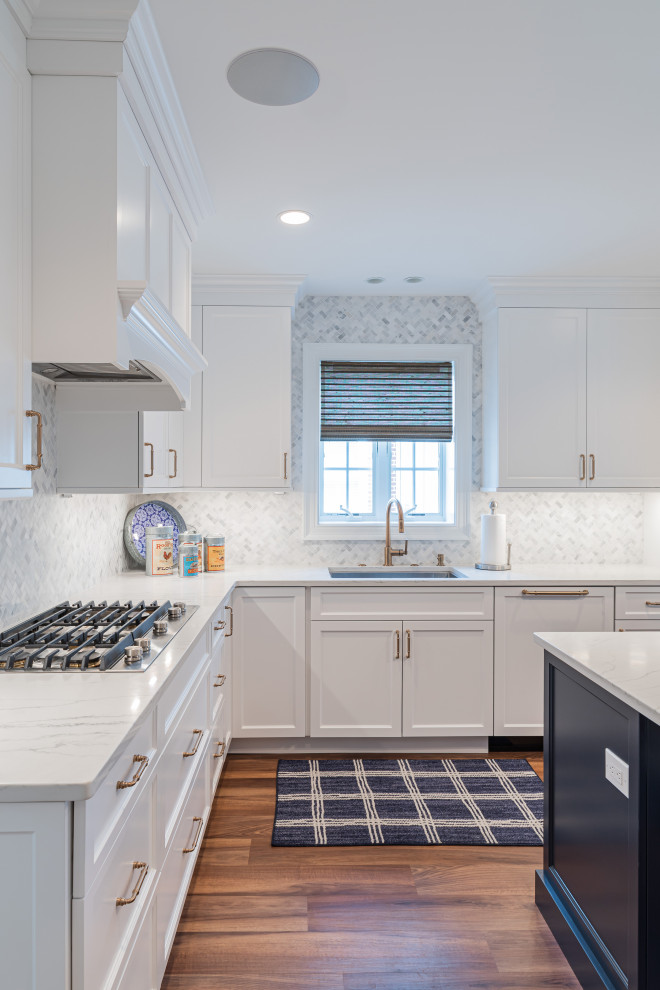 Large coastal u-shaped kitchen/diner in Philadelphia with a submerged sink, shaker cabinets, white cabinets, engineered stone countertops, white splashback, marble splashback, integrated appliances, vinyl flooring, an island, brown floors and white worktops.