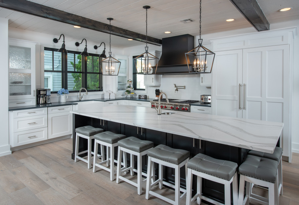Transitional l-shaped medium tone wood floor and brown floor kitchen photo in Philadelphia with a farmhouse sink, recessed-panel cabinets, white cabinets, white backsplash, subway tile backsplash, stainless steel appliances, an island and white countertops