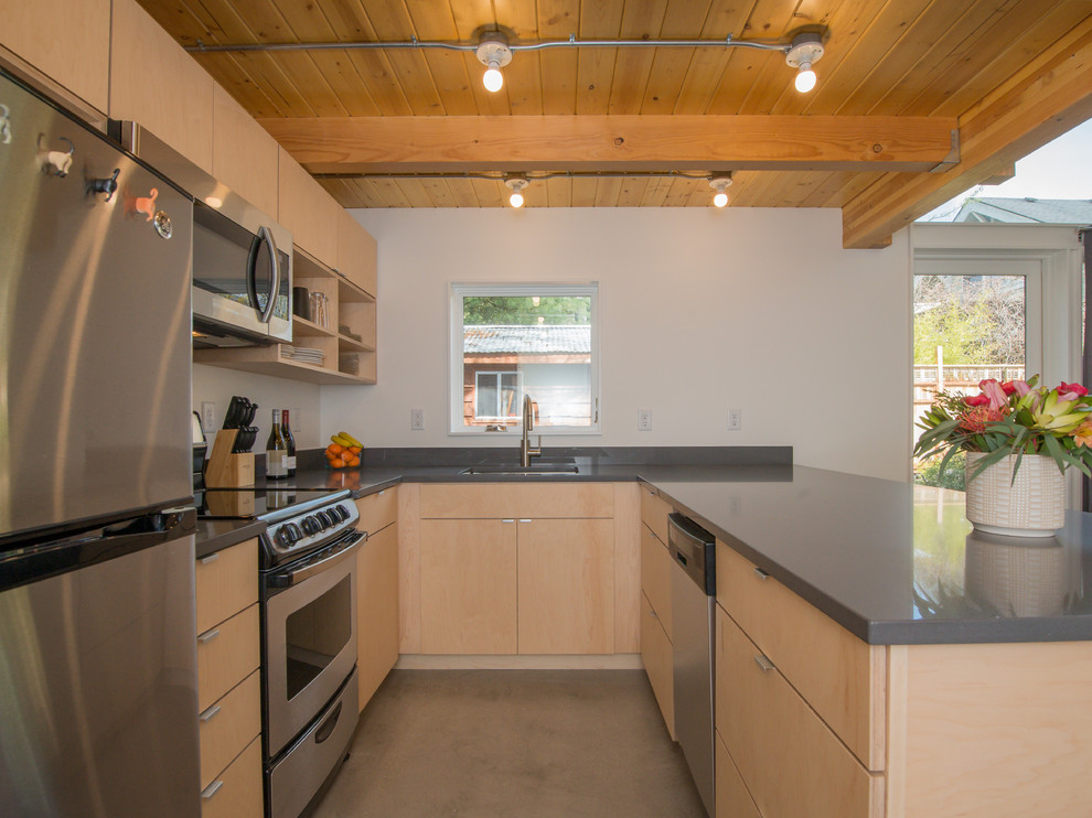 Medium sized modern l-shaped open plan kitchen in Portland with a submerged sink, flat-panel cabinets, light wood cabinets, composite countertops, stainless steel appliances, concrete flooring, a breakfast bar, grey floors and grey worktops.