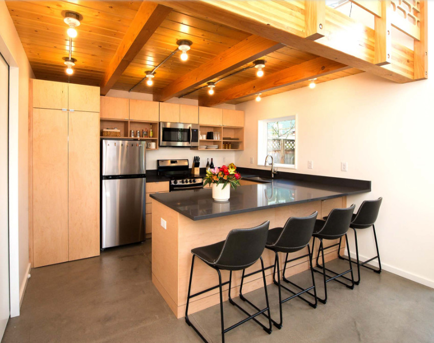 This is an example of a medium sized traditional u-shaped open plan kitchen in Portland with a submerged sink, flat-panel cabinets, light wood cabinets, engineered stone countertops, stainless steel appliances, concrete flooring, a breakfast bar, grey floors and black worktops.