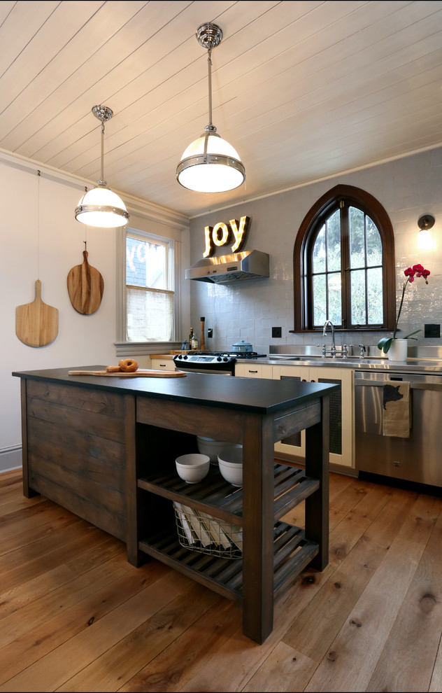 Inspiration for a small eclectic single-wall open plan kitchen in Portland with an integrated sink, shaker cabinets, white cabinets, stainless steel worktops, grey splashback, ceramic splashback, stainless steel appliances and medium hardwood flooring.