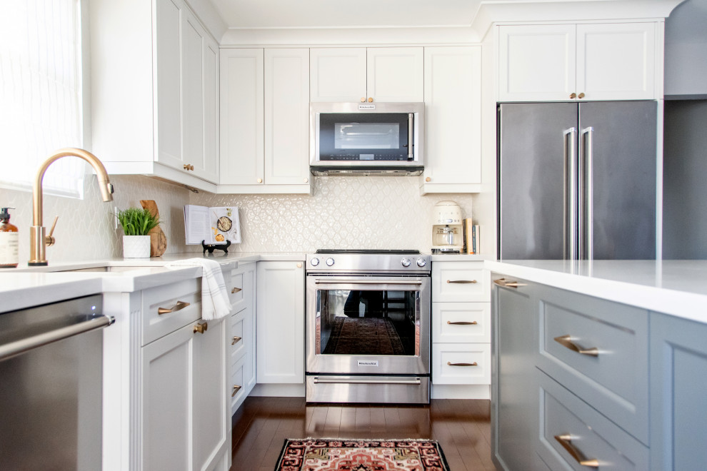 Foto på ett mellanstort vintage grå kök, med en undermonterad diskho, skåp i shakerstil, vita skåp, bänkskiva i kvartsit, vitt stänkskydd, stänkskydd i mosaik, rostfria vitvaror, mellanmörkt trägolv, en köksö och brunt golv