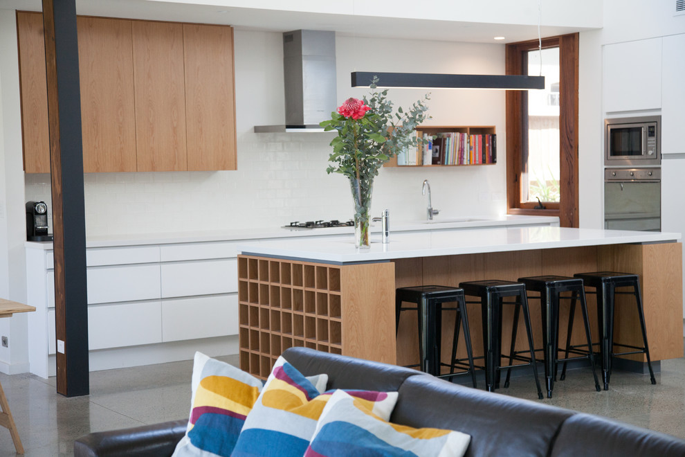 Bild på ett stort funkis linjärt kök och matrum, med en dubbel diskho, vita skåp, vitt stänkskydd, rostfria vitvaror, betonggolv och en köksö