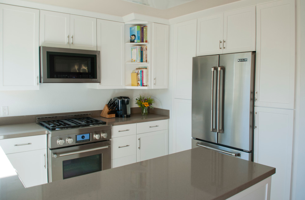 Ejemplo de cocina actual con armarios estilo shaker, puertas de armario blancas, encimera de cuarzo compacto, electrodomésticos de acero inoxidable y península