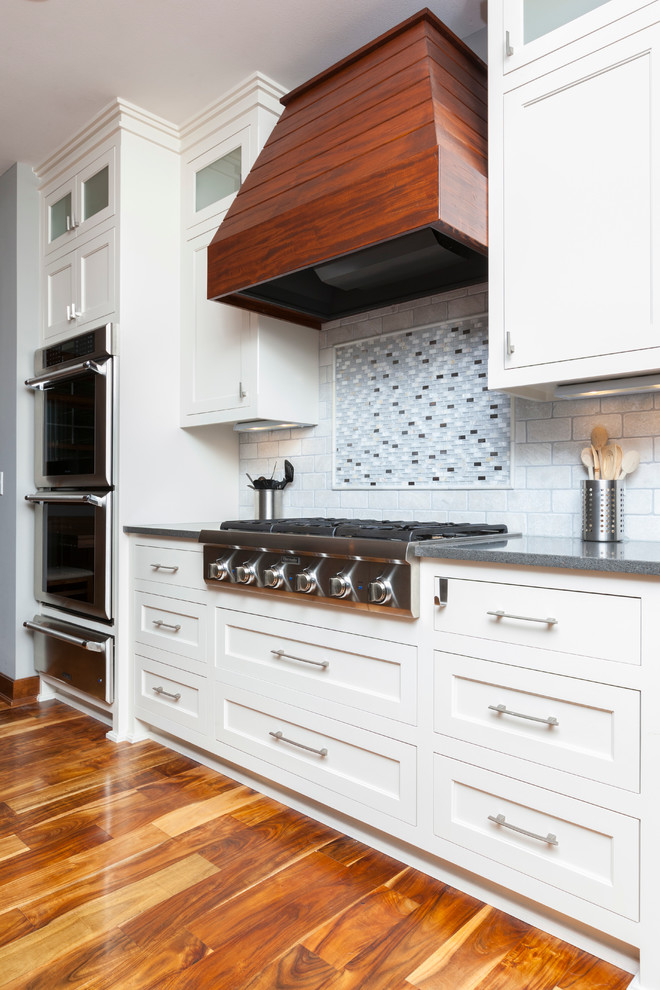 Example of a mid-sized arts and crafts l-shaped medium tone wood floor eat-in kitchen design in Milwaukee with an undermount sink, flat-panel cabinets, white cabinets, wood countertops, white backsplash, ceramic backsplash, stainless steel appliances and an island