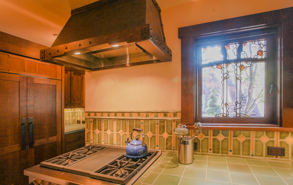 На фото: отдельная, п-образная кухня в стиле кантри с с полувстраиваемой мойкой (с передним бортиком), темными деревянными фасадами, столешницей из плитки, зеленым фартуком, фартуком из керамической плитки и техникой под мебельный фасад