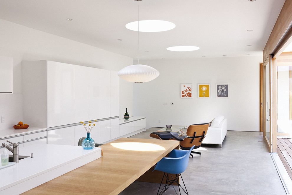 Стильный дизайн: прямая кухня-гостиная в стиле модернизм с плоскими фасадами, белыми фасадами, столешницей из кварцевого агломерата, белым фартуком, бетонным полом и островом - последний тренд