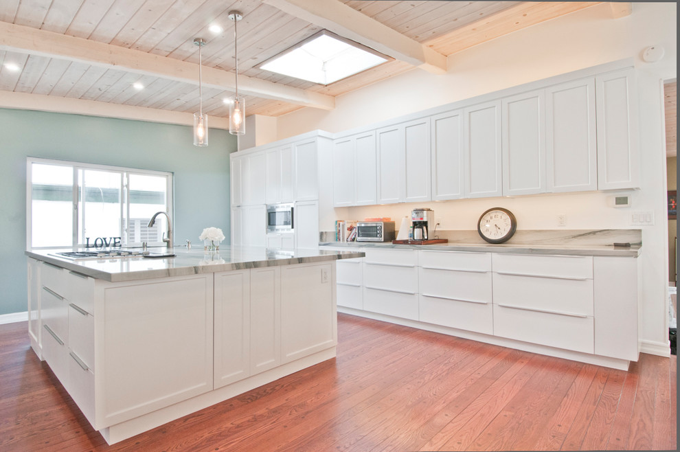 Modern inredning av ett stort kök, med en dubbel diskho, luckor med infälld panel, vita skåp, marmorbänkskiva, stänkskydd i sten, rostfria vitvaror och mellanmörkt trägolv