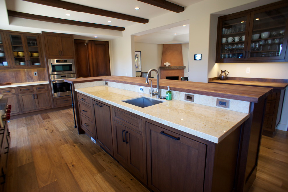Traditional galley enclosed kitchen in Santa Barbara with a double-bowl sink, shaker cabinets, medium wood cabinets, limestone worktops, porcelain splashback, integrated appliances, light hardwood flooring and an island.