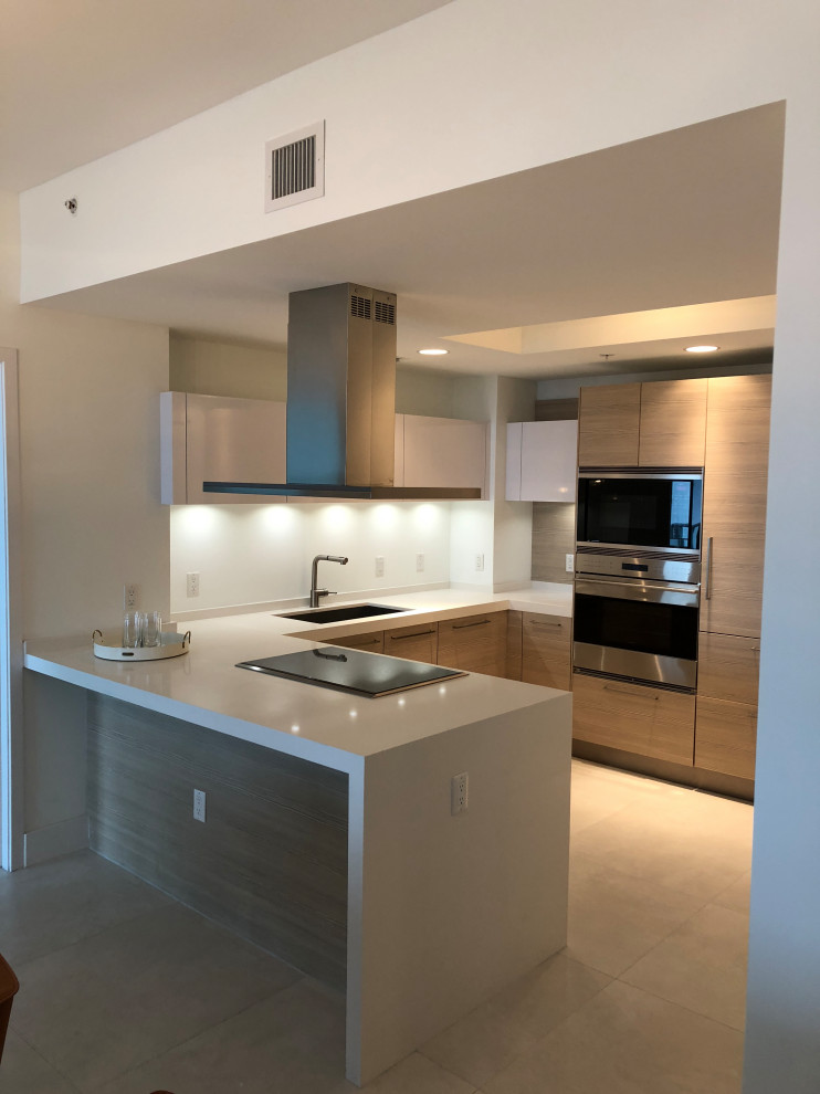 Small modern u-shaped kitchen/diner in Miami with a submerged sink, flat-panel cabinets, white cabinets, quartz worktops, stainless steel appliances, porcelain flooring, a breakfast bar, beige floors and white worktops.