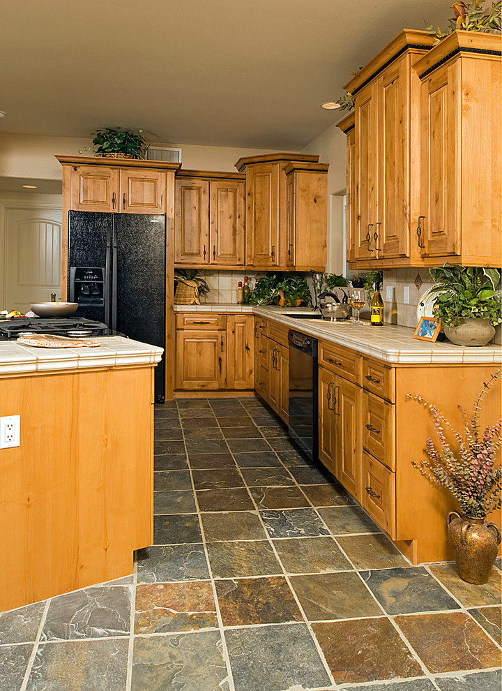 Foto på ett litet rustikt kök, med en undermonterad diskho, luckor med upphöjd panel, skåp i mellenmörkt trä, kaklad bänkskiva, beige stänkskydd, stänkskydd i porslinskakel, svarta vitvaror, skiffergolv och en köksö