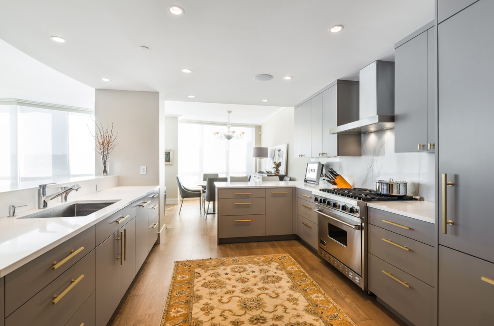 Inspiration for a medium sized contemporary open plan kitchen in Vancouver with engineered stone countertops, grey splashback, marble splashback, a submerged sink, flat-panel cabinets, grey cabinets, stainless steel appliances, medium hardwood flooring, a breakfast bar and brown floors.