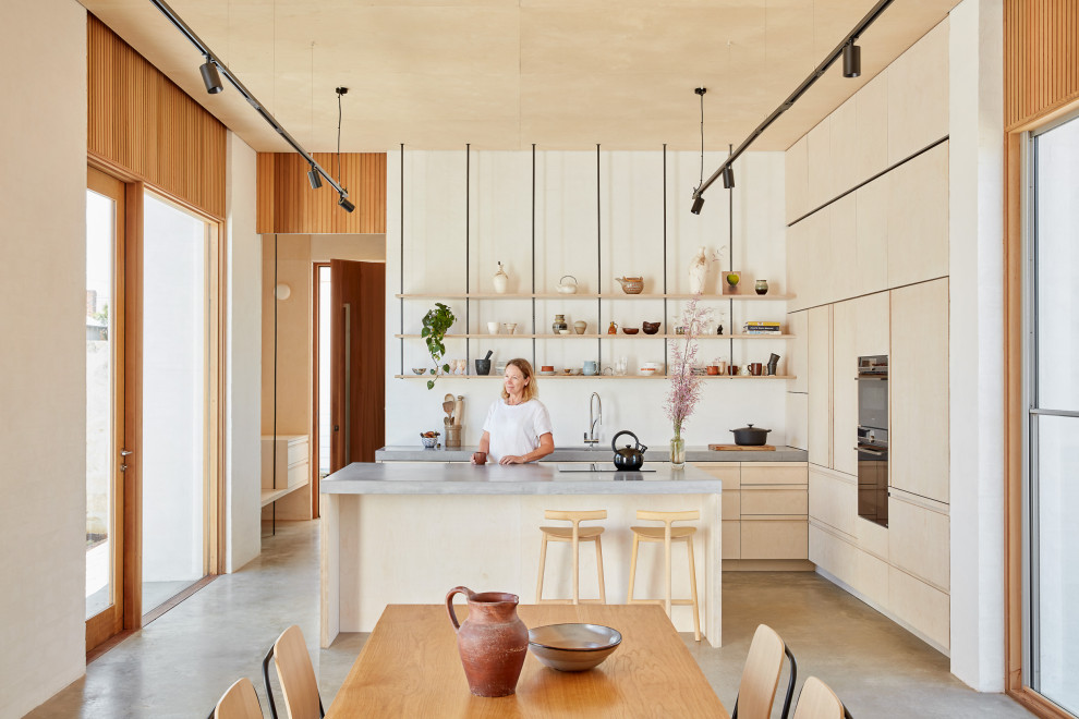 Foto på ett mellanstort funkis grå kök, med bänkskiva i betong, betonggolv, en köksö, grått golv, en undermonterad diskho, släta luckor, skåp i ljust trä och integrerade vitvaror