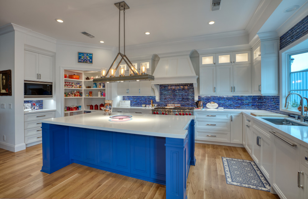 This is an example of a large traditional u-shaped kitchen/diner in Los Angeles with a submerged sink, recessed-panel cabinets, white cabinets, marble worktops, blue splashback, matchstick tiled splashback, stainless steel appliances, an island, white worktops, medium hardwood flooring and brown floors.