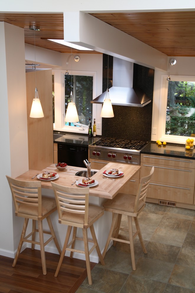 Example of a trendy galley eat-in kitchen design in Vancouver with an undermount sink, flat-panel cabinets, light wood cabinets, granite countertops, black backsplash, stone slab backsplash and stainless steel appliances