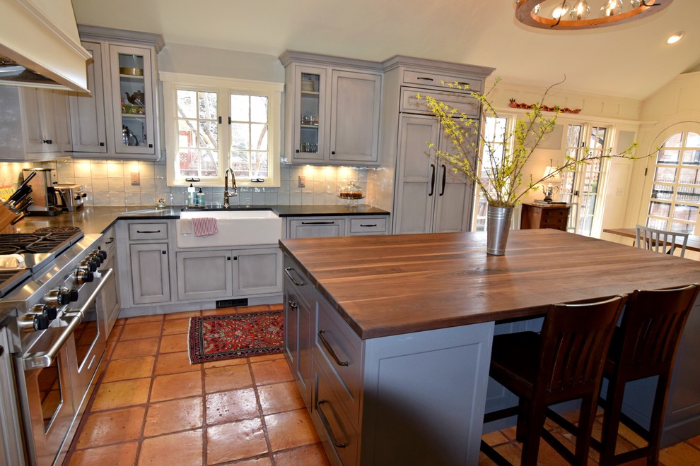 Exempel på ett klassiskt kök, med en rustik diskho, luckor med infälld panel, grå skåp, träbänkskiva, grått stänkskydd, stänkskydd i glaskakel, integrerade vitvaror, klinkergolv i terrakotta och en köksö