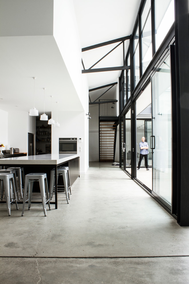 Свежая идея для дизайна: огромная параллельная кухня-гостиная в стиле модернизм с темными деревянными фасадами, столешницей из кварцевого агломерата, фартуком из металлической плитки, техникой из нержавеющей стали, бетонным полом и островом - отличное фото интерьера