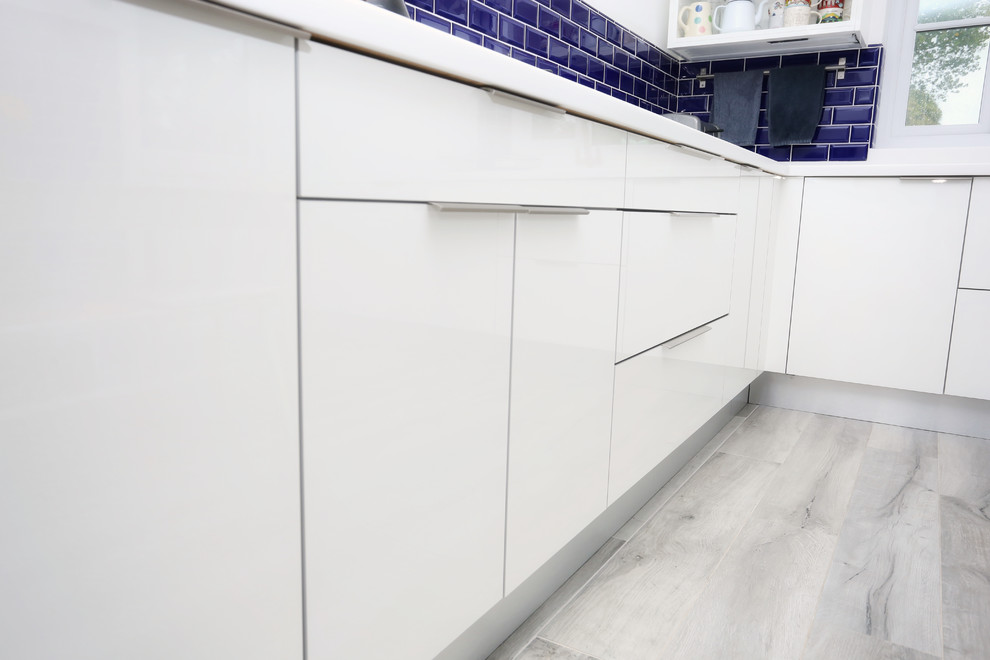 Inspiration for a medium sized contemporary u-shaped enclosed kitchen in Other with an integrated sink, flat-panel cabinets, white cabinets, composite countertops, blue splashback, ceramic splashback, black appliances and white worktops.