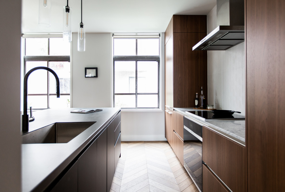 Photo of a modern kitchen/diner in Seattle with a submerged sink, flat-panel cabinets, dark wood cabinets, composite countertops, white splashback, ceramic splashback, integrated appliances, medium hardwood flooring, an island, brown floors and grey worktops.