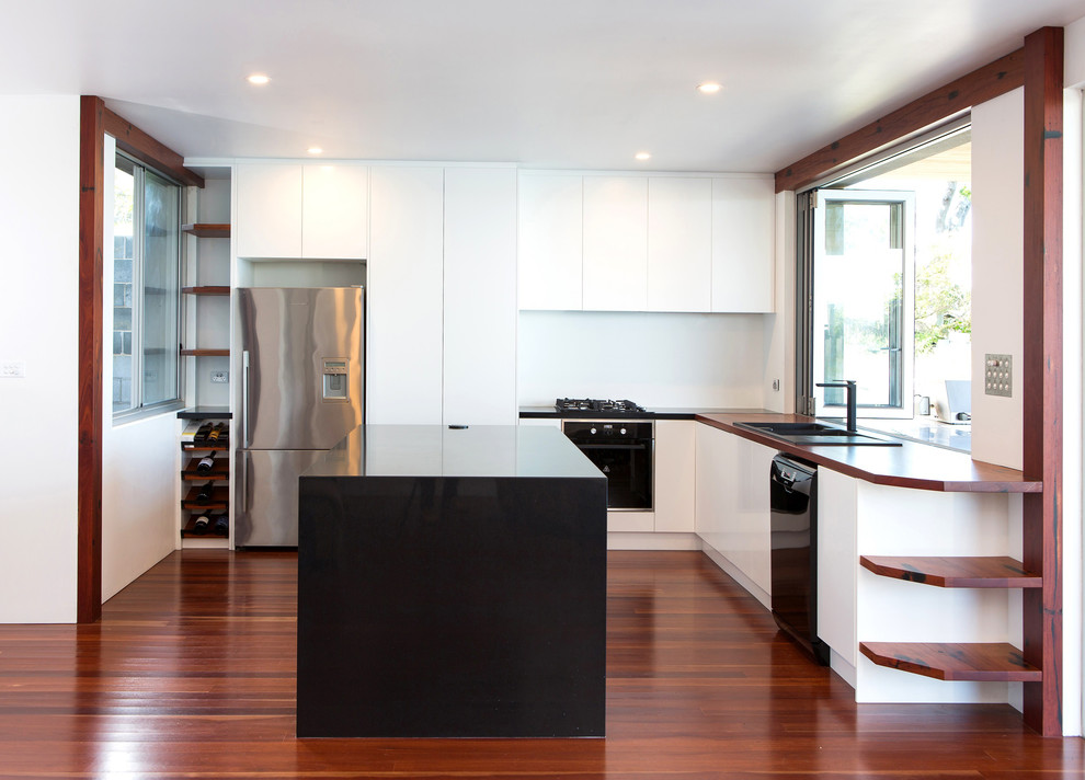 Modern inredning av ett mellanstort u-kök, med en dubbel diskho, träbänkskiva, vitt stänkskydd, svarta vitvaror, mellanmörkt trägolv och en köksö