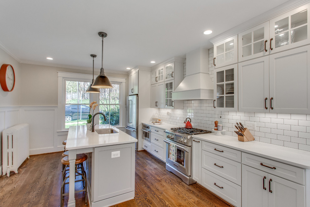 Idéer för att renovera ett stort amerikanskt vit linjärt vitt kök och matrum, med en undermonterad diskho, skåp i shakerstil, vita skåp, bänkskiva i kvarts, vitt stänkskydd, stänkskydd i keramik, rostfria vitvaror, mellanmörkt trägolv, en köksö och brunt golv