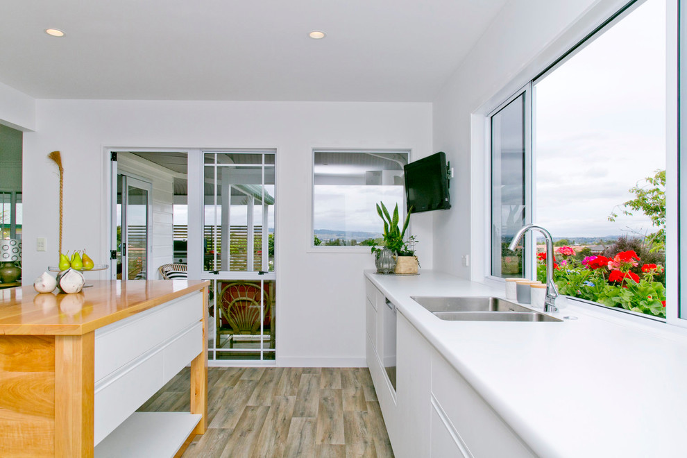Immagine di una cucina minimalista chiusa e di medie dimensioni con ante bianche, elettrodomestici in acciaio inossidabile, pavimento in vinile e top bianco