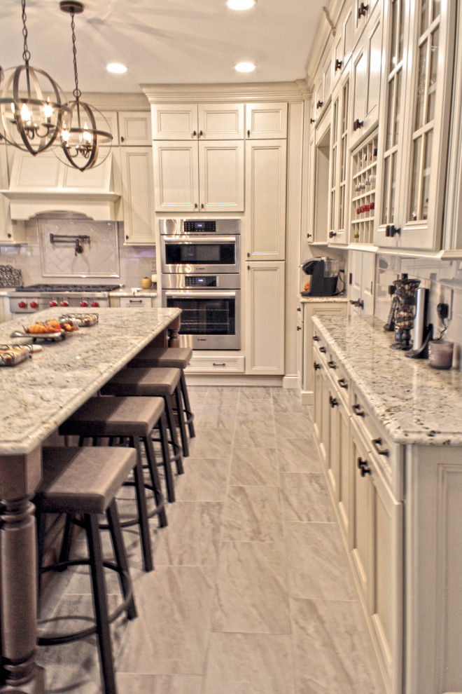 Large transitional u-shaped ceramic tile and gray floor open concept kitchen photo in Philadelphia with an undermount sink, recessed-panel cabinets, distressed cabinets, granite countertops, gray backsplash, porcelain backsplash, stainless steel appliances, an island and multicolored countertops