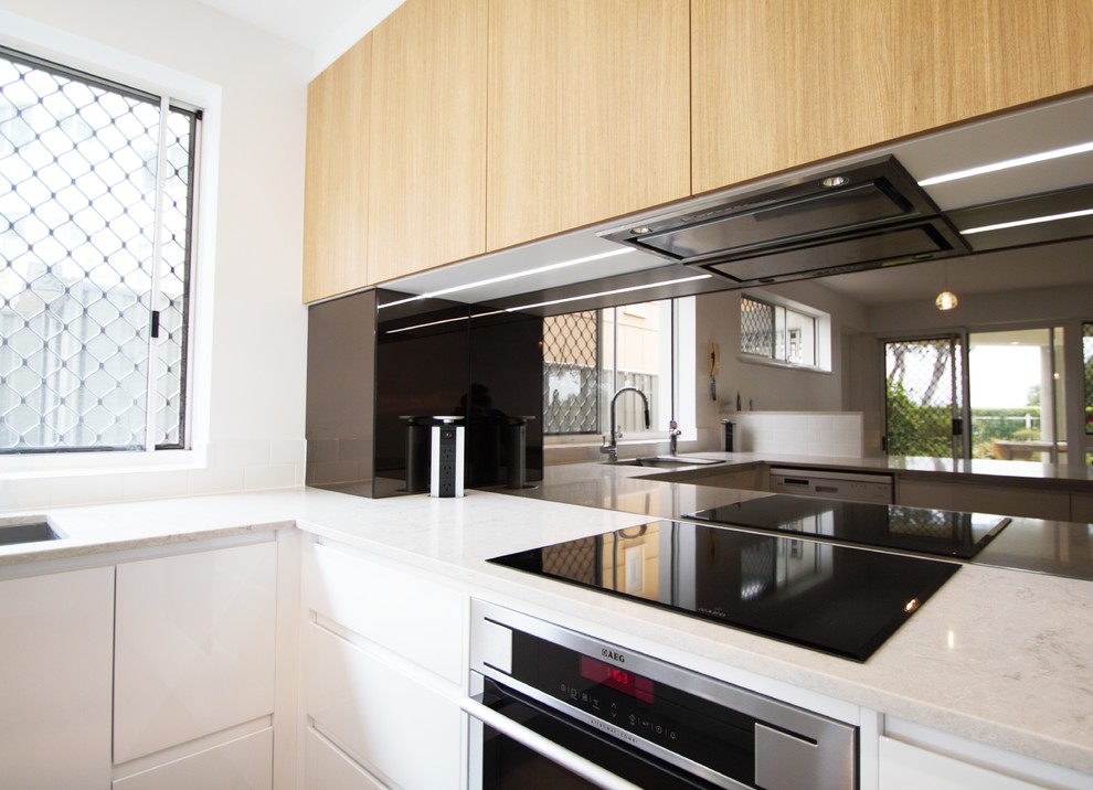 Idéer för att renovera ett mellanstort funkis grå grått kök, med en undermonterad diskho, vita skåp, bänkskiva i kvarts, stänkskydd med metallisk yta, spegel som stänkskydd, rostfria vitvaror och en halv köksö