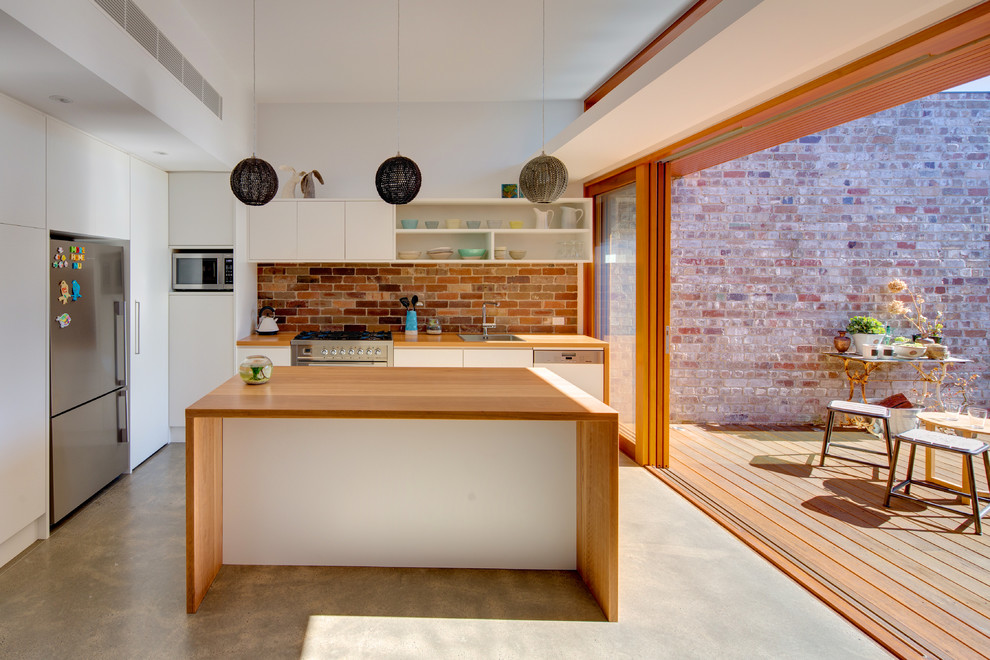 Imagen de cocina moderna con una isla, armarios con paneles lisos, puertas de armario blancas, encimera de madera y suelo de cemento