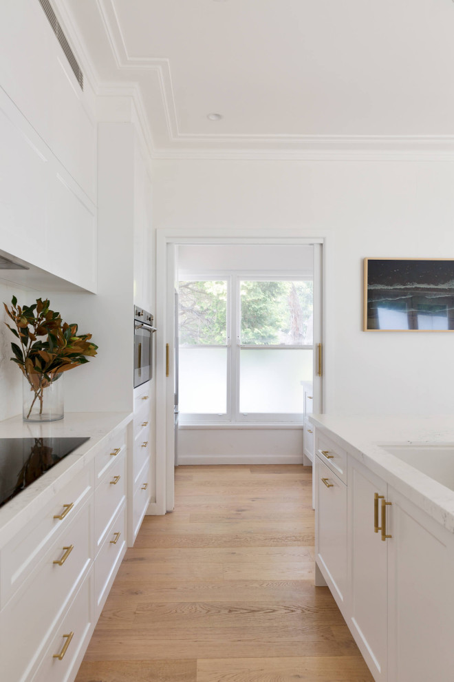 Inredning av ett modernt mellanstort vit vitt skafferi, med en nedsänkt diskho, luckor med infälld panel, vita skåp, bänkskiva i koppar, vitt stänkskydd, stänkskydd i sten, rostfria vitvaror, ljust trägolv, en köksö och beiget golv