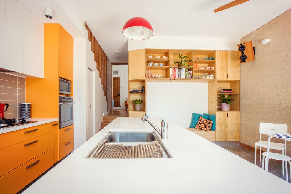 Свежая идея для дизайна: параллельная кухня-гостиная среднего размера в стиле фьюжн с врезной мойкой, оранжевыми фасадами, гранитной столешницей, белой техникой, бетонным полом, островом и серым полом - отличное фото интерьера