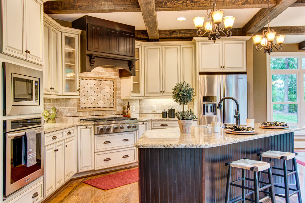 Bild på ett stort vintage kök, med en undermonterad diskho, luckor med upphöjd panel, beige skåp, granitbänkskiva, beige stänkskydd, stänkskydd i stenkakel, rostfria vitvaror, mellanmörkt trägolv, en köksö och brunt golv