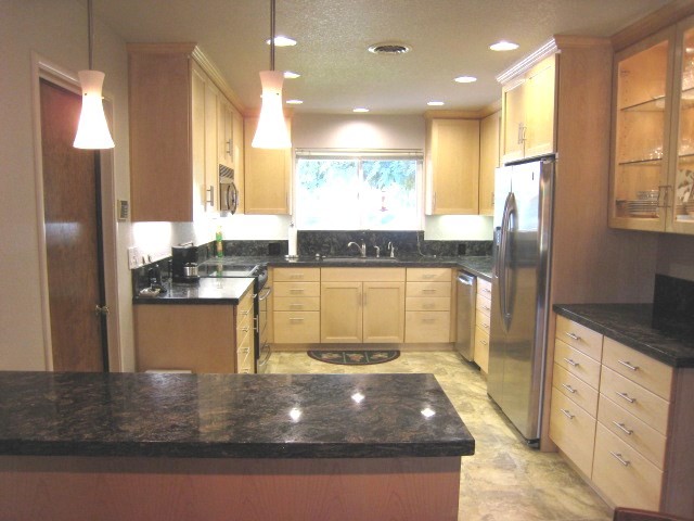 Bild på ett mellanstort funkis kök, med en undermonterad diskho, skåp i shakerstil, skåp i mellenmörkt trä, granitbänkskiva, svart stänkskydd, stänkskydd i sten, rostfria vitvaror och klinkergolv i porslin