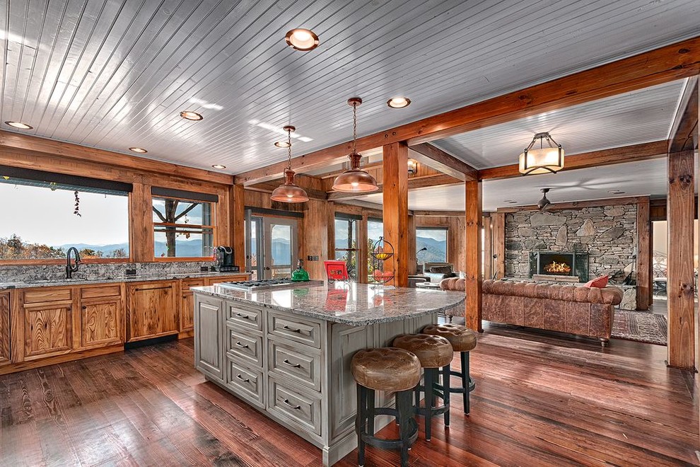 Foto på ett rustikt kök med öppen planlösning, med skåp i mellenmörkt trä, grått stänkskydd, mörkt trägolv, en köksö, brunt golv och luckor med upphöjd panel