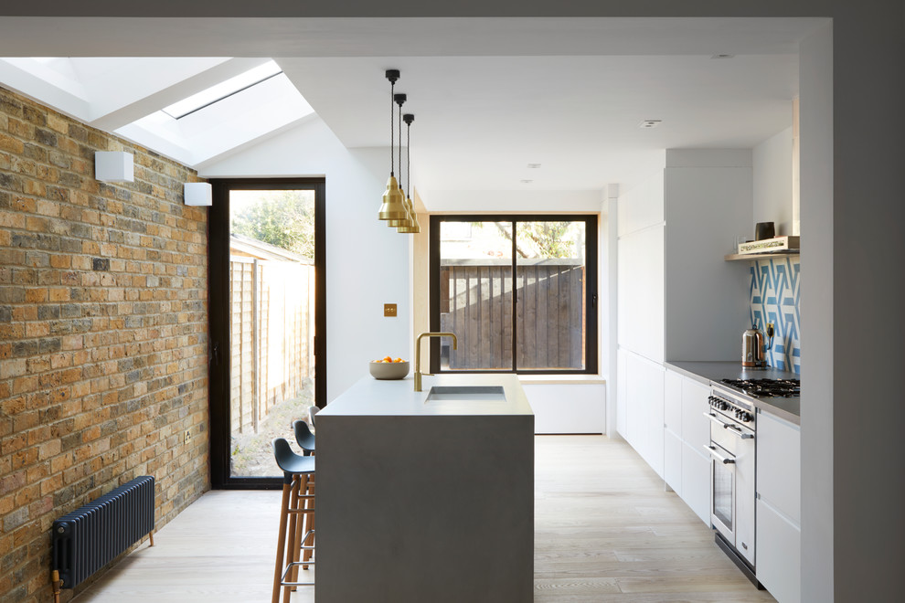Bild på ett mellanstort funkis grå grått kök, med en undermonterad diskho, släta luckor, vita skåp, bänkskiva i betong, flerfärgad stänkskydd, stänkskydd i cementkakel, rostfria vitvaror, ljust trägolv och en köksö
