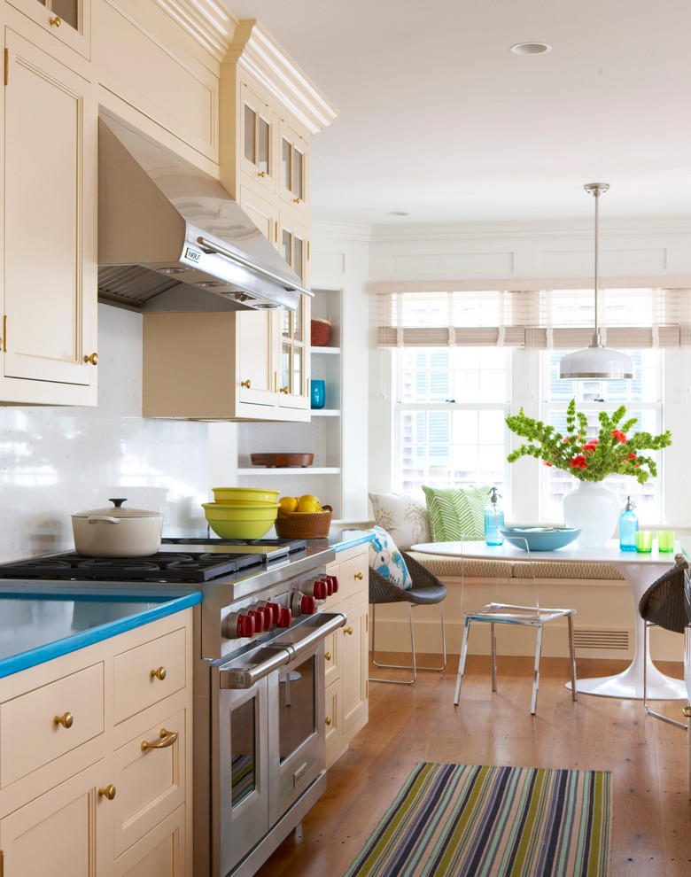 Example of a beach style eat-in kitchen design in New York with recessed-panel cabinets, beige cabinets, white backsplash and turquoise countertops