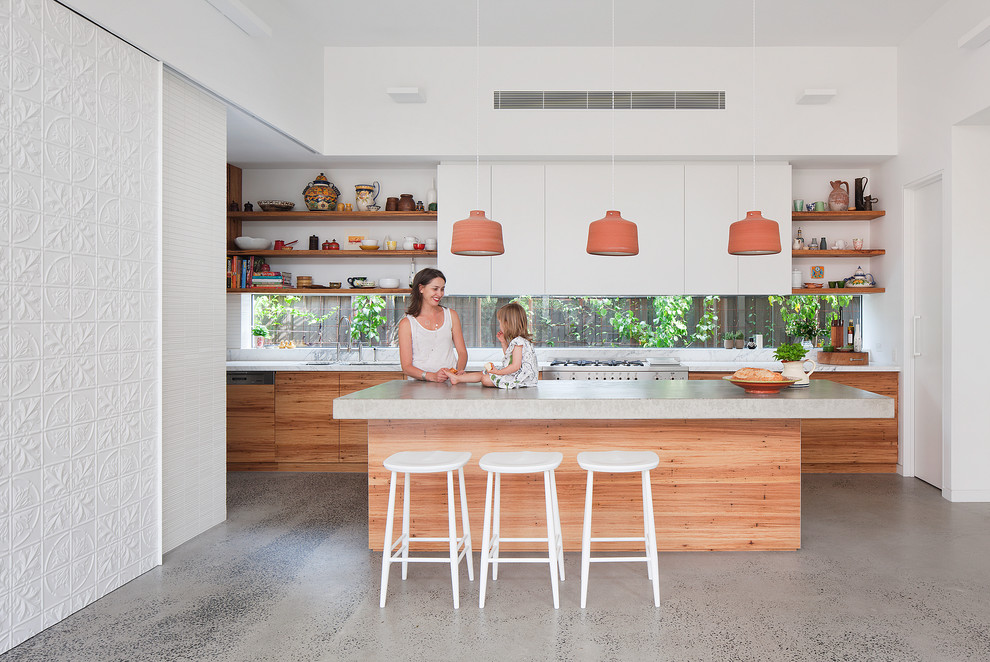 This is an example of a medium sized contemporary galley kitchen in Melbourne with a submerged sink, flat-panel cabinets, white cabinets, concrete worktops, glass sheet splashback, stainless steel appliances, concrete flooring and an island.