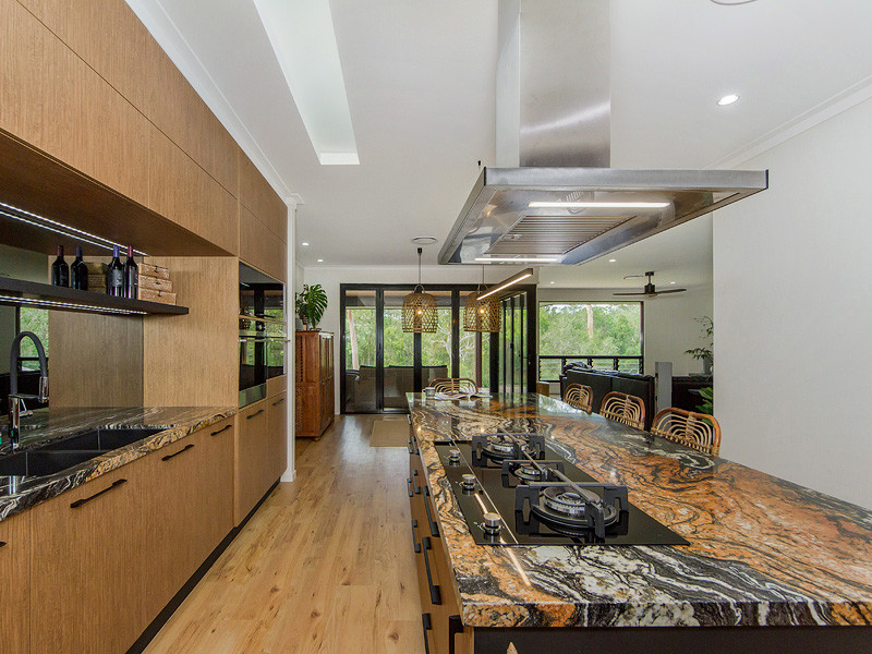 Contemporary kitchen in Brisbane with a submerged sink, medium wood cabinets, granite worktops, mirror splashback, black appliances, vinyl flooring and an island.