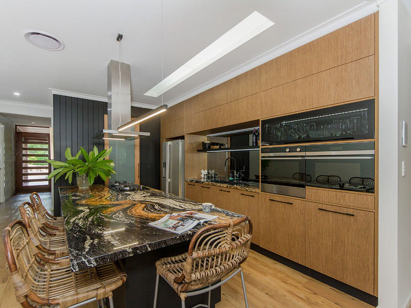Photo of a contemporary kitchen in Brisbane with a submerged sink, medium wood cabinets, granite worktops, mirror splashback, black appliances, vinyl flooring and an island.