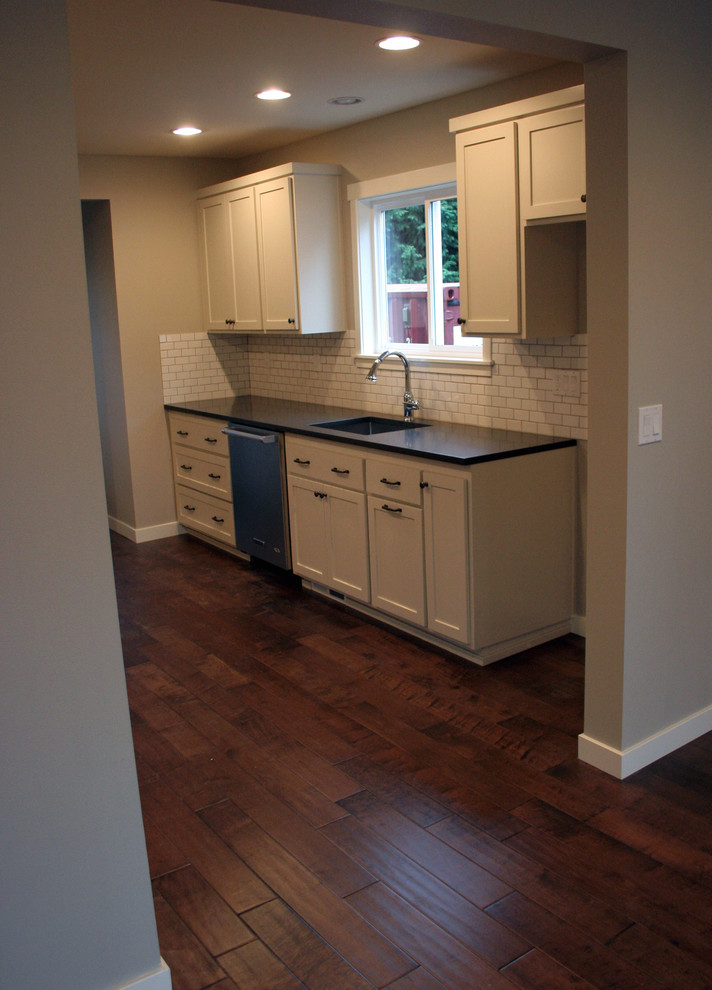 Example of a small arts and crafts galley medium tone wood floor open concept kitchen design in Portland with an undermount sink, shaker cabinets, white cabinets, quartz countertops, white backsplash, ceramic backsplash and stainless steel appliances