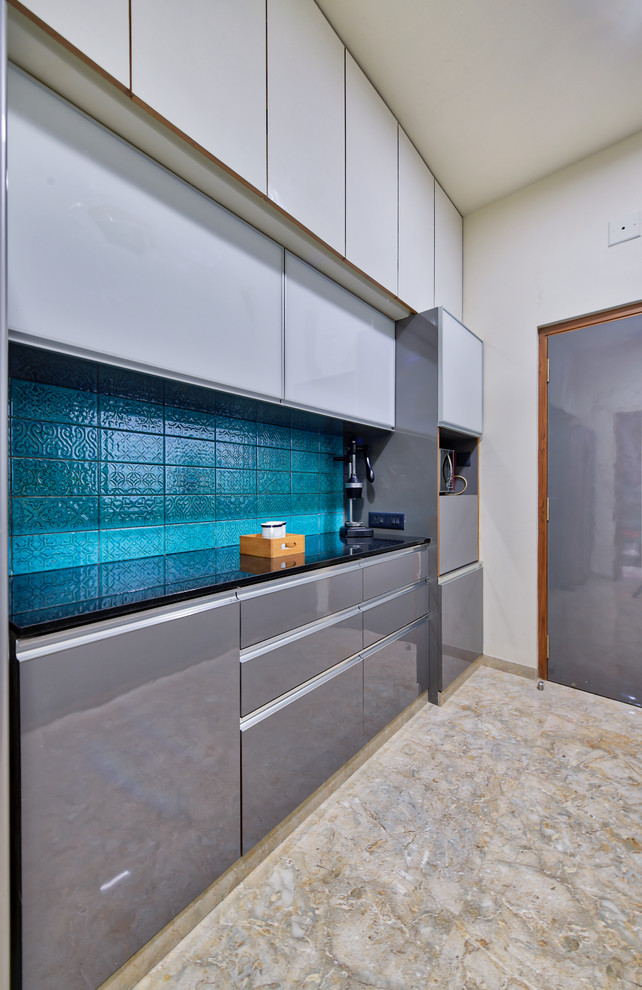 Moderne Küche mit flächenbündigen Schrankfronten, grauen Schränken, Küchenrückwand in Blau, Rückwand aus Keramikfliesen, braunem Boden und schwarzer Arbeitsplatte in Ahmedabad