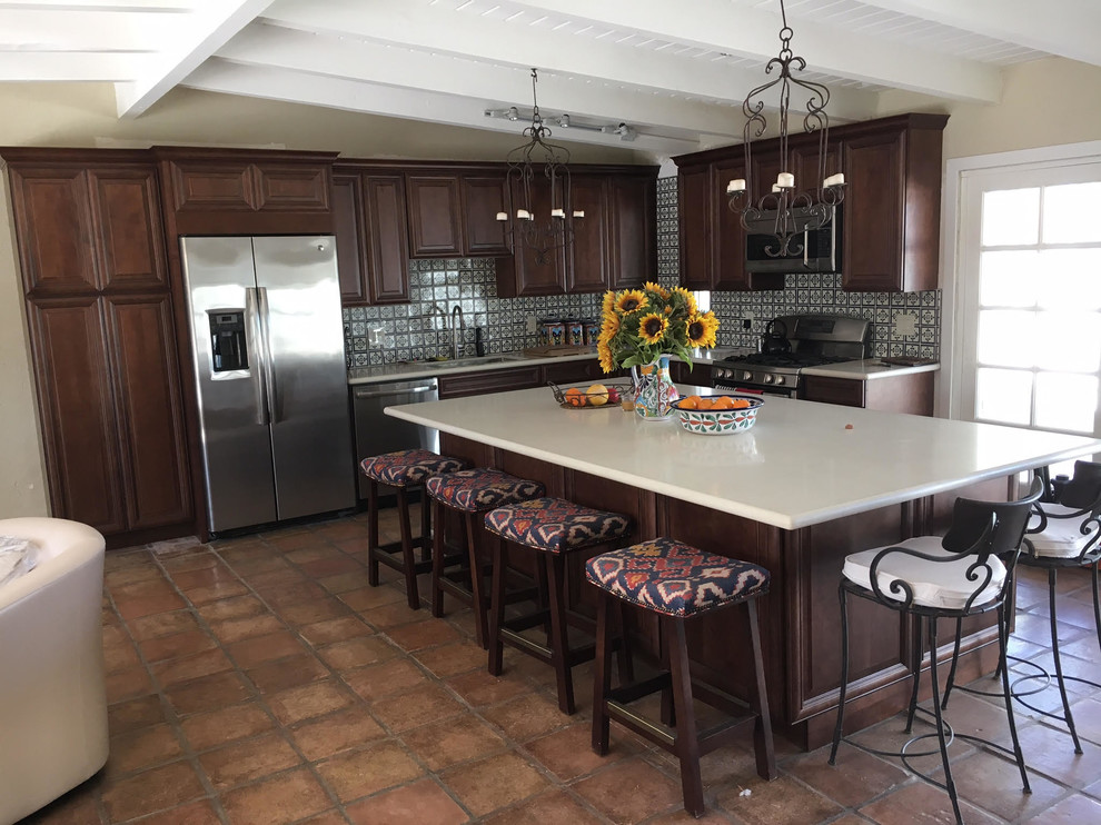 Inredning av ett medelhavsstil mellanstort vit vitt kök, med en undermonterad diskho, luckor med upphöjd panel, skåp i mörkt trä, bänkskiva i koppar, flerfärgad stänkskydd, stänkskydd i keramik, rostfria vitvaror, klinkergolv i terrakotta, en köksö och orange golv