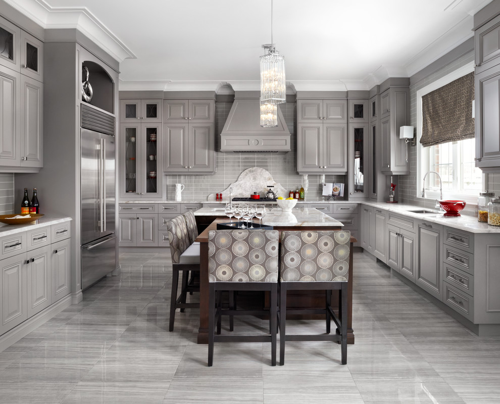 Klassisk inredning av ett u-kök, med en undermonterad diskho, luckor med upphöjd panel, grå skåp, grått stänkskydd, rostfria vitvaror och en köksö