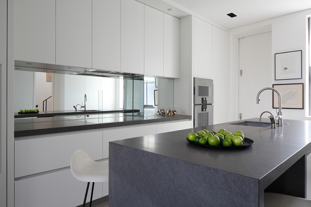 Design ideas for a small contemporary single-wall kitchen in London with a submerged sink, flat-panel cabinets, mirror splashback, white appliances and a breakfast bar.